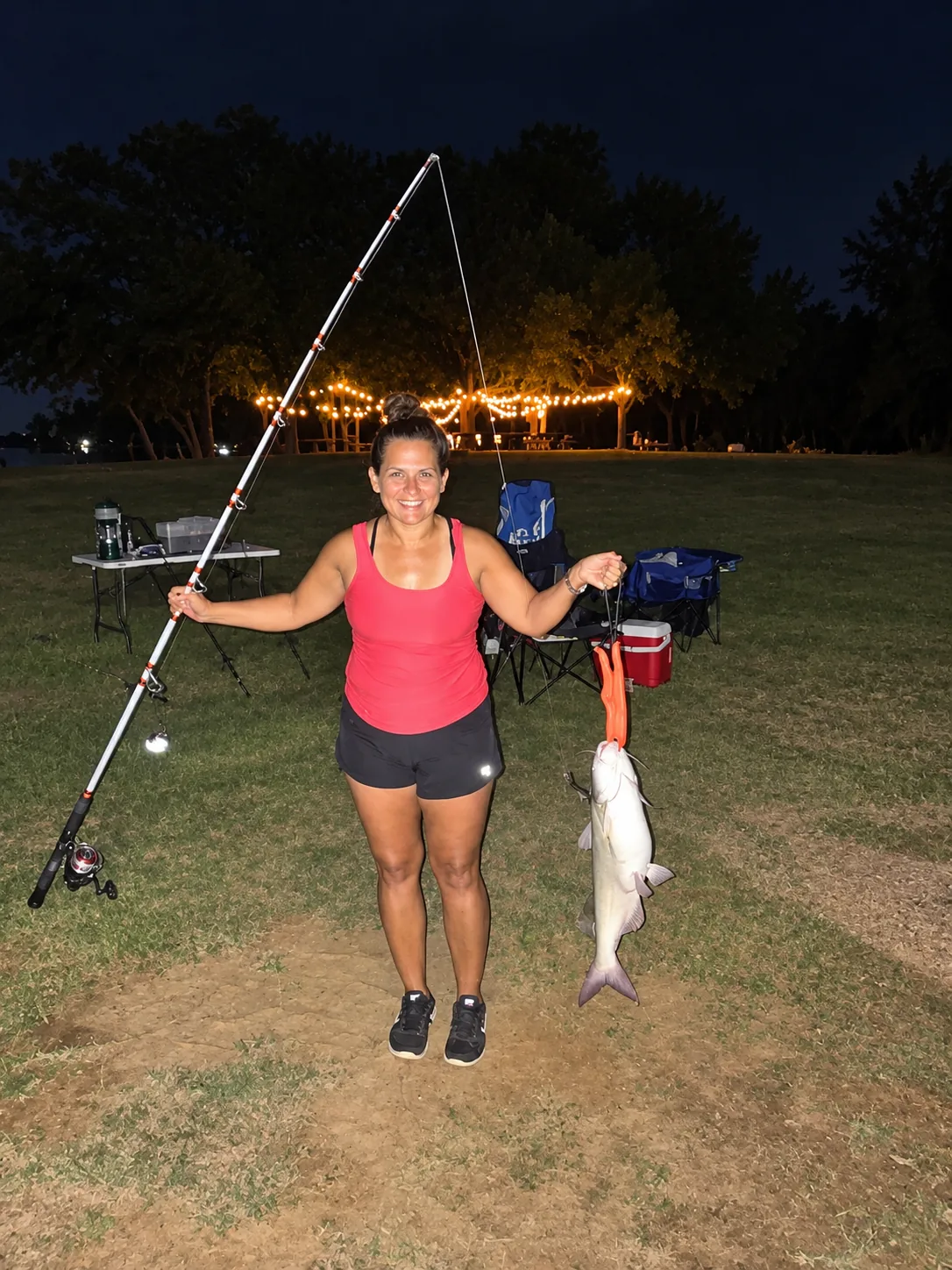 A guest holding up a catfish caught at Waterfront Hideaway Ranch, with the bistro lights on behind her